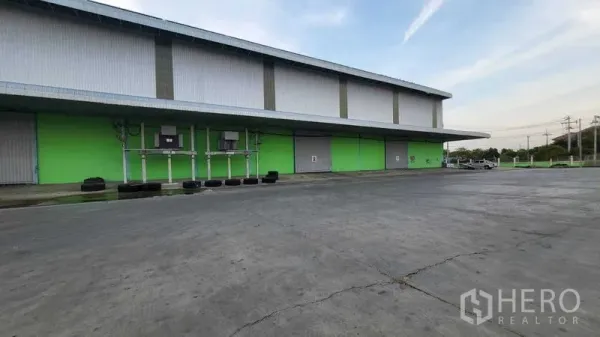 โรงงาน ให้เช่าในSai Noi, Nonthaburi - ด้านข้างอาคารผนังสีเขียว มีประตูม้วนหลายจุด ระบบสาธารณูปโภค และลานกว้าง