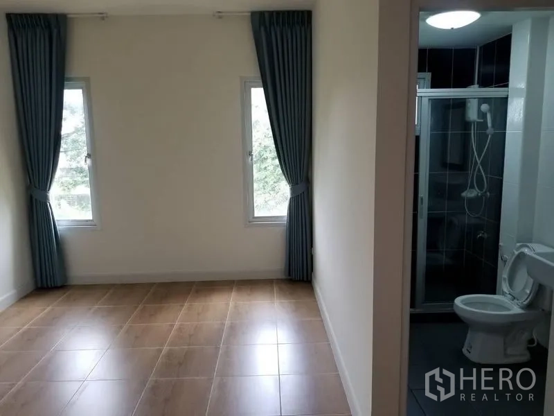 Townhouse for rent in Bang Kapi, Bangkok - Bedroom with blue curtains beside an en-suite bathroom with glass shower.