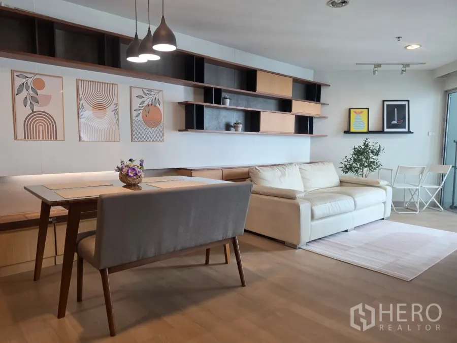 Condominium for rent in Huai Khwang, Bangkok - Bright living room with white sofa, open shelving, and large glass door to balcony.