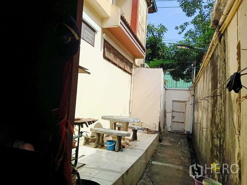บ้าน ขายในBang Na, Bangkok - เฉลียงข้างบ้านปูกระเบื้องพร้อมโต๊ะหินอ่อนและประตูรั้ว ระหว่างกำแพงบ้าน