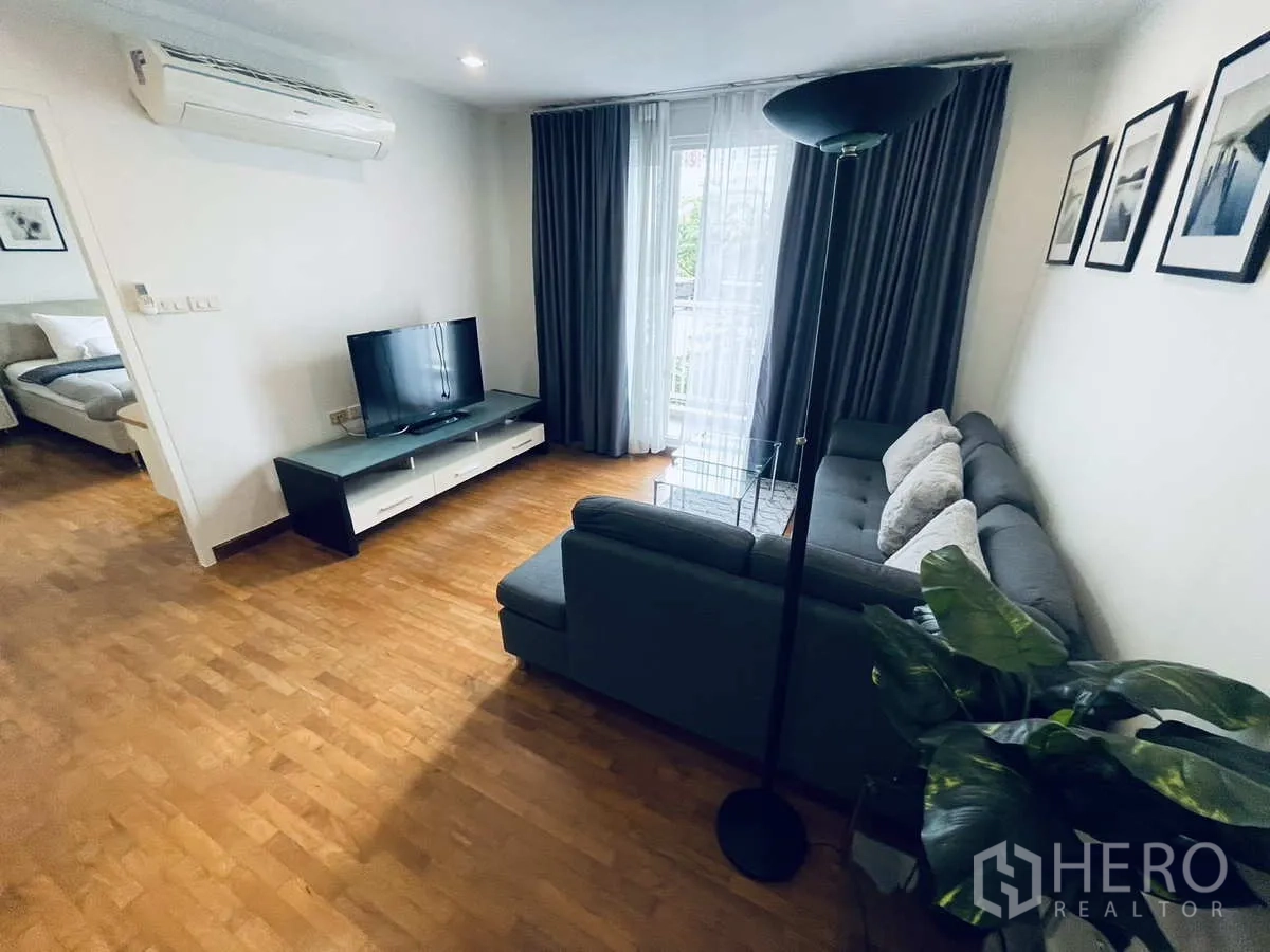 คอนโด ให้เช่าในWatthana, Bangkok - ห้องนั่งเล่นสว่าง โซฟาเข้ามุมสีเทา ชั้นวางทีวี พื้นไม้ และผ้าม่านระเบียง