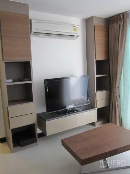 Condominium for rent in Khlong Toei, Bangkok - Built-in media wall with shelving, air conditioner, and flat-screen TV beside full-height curtains.