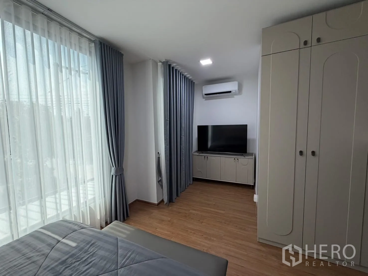 联排别墅 for rent in Bang Phli, Samut Prakan - 主卧一角，电视柜、空调、衣柜与长窗及灰色窗帘。