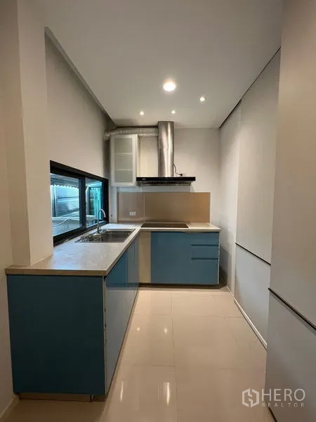 Detached House for rent in Saphan Sung, Bangkok - Fitted kitchen with blue lower cabinets, countertops, sink and stainless range hood.