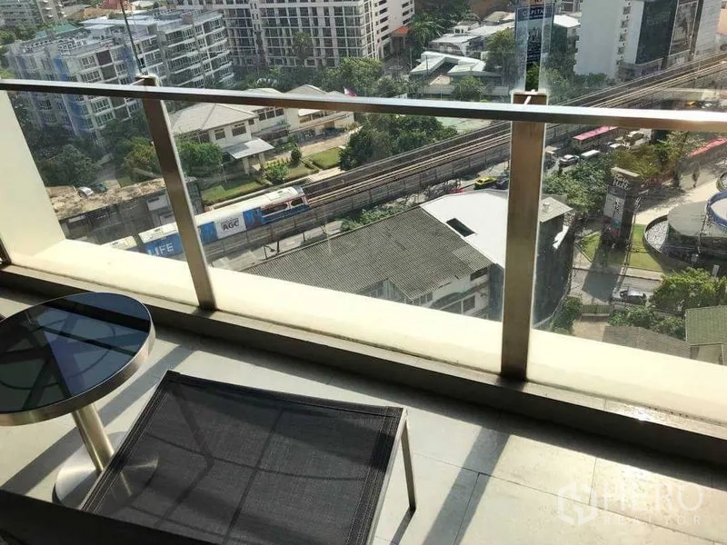 Condominium for rent in Watthana, Bangkok - Private balcony with glass railing, outdoor table and chair overlooking city skyline and the BTS Thonglor track.