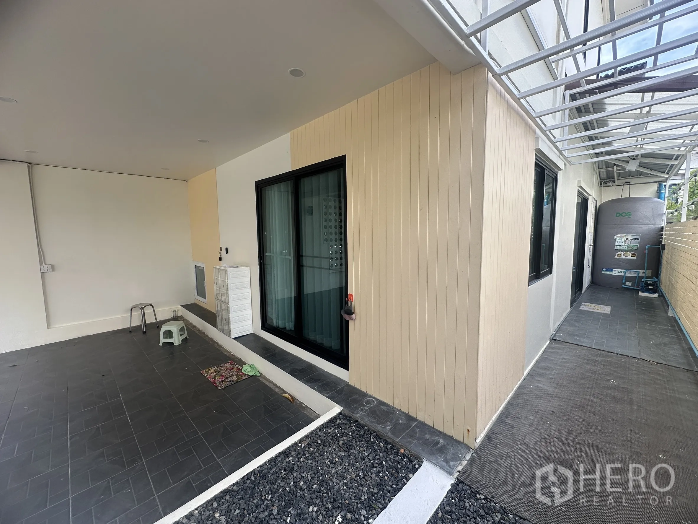 Townhouse for sale in Lam Luk Ka, Pathum Thani - Side walkway with roof structure, privacy fence, and a water tank.