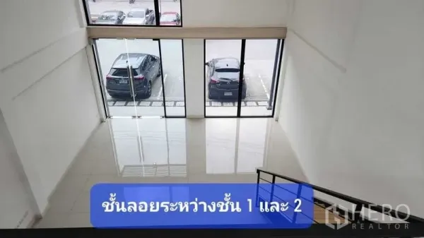 Townhouse for rent in Bueng Kum, Bangkok - Double-height front hall with floor-to-ceiling glass and view of parking area, seen from the mezzanine stairs.
