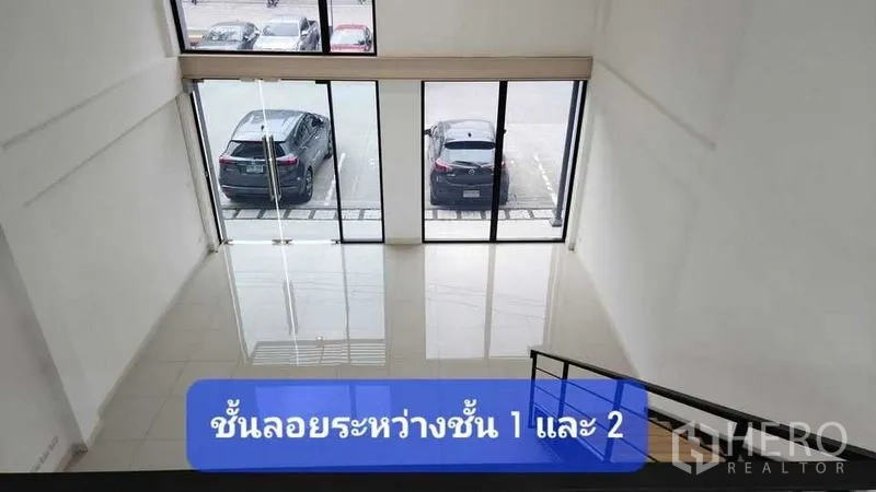 Townhouse for rent in Bueng Kum, Bangkok - Double-height front hall with floor-to-ceiling glass and view of parking area, seen from the mezzanine stairs.
