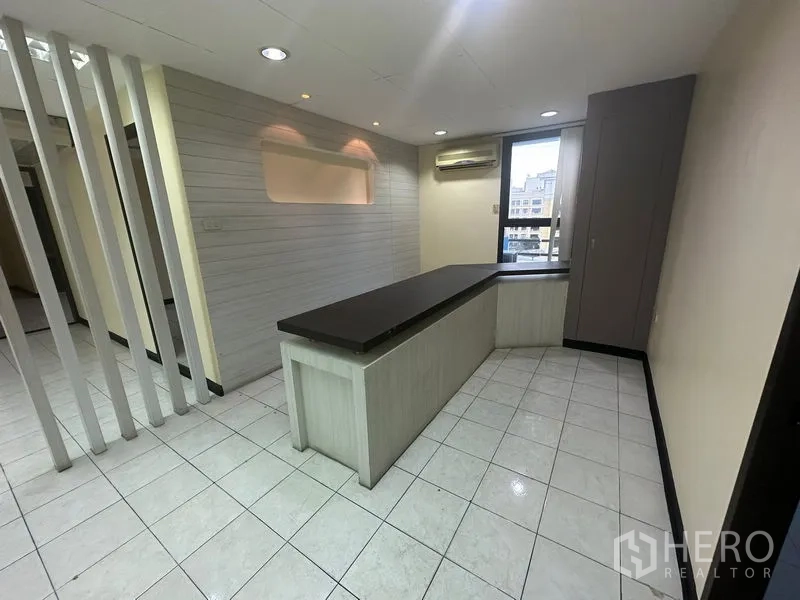 Office Space for rent in Bang Rak, Bangkok - Reception-style area with built-in counter, tiled floors, accent wall and a window air conditioner.