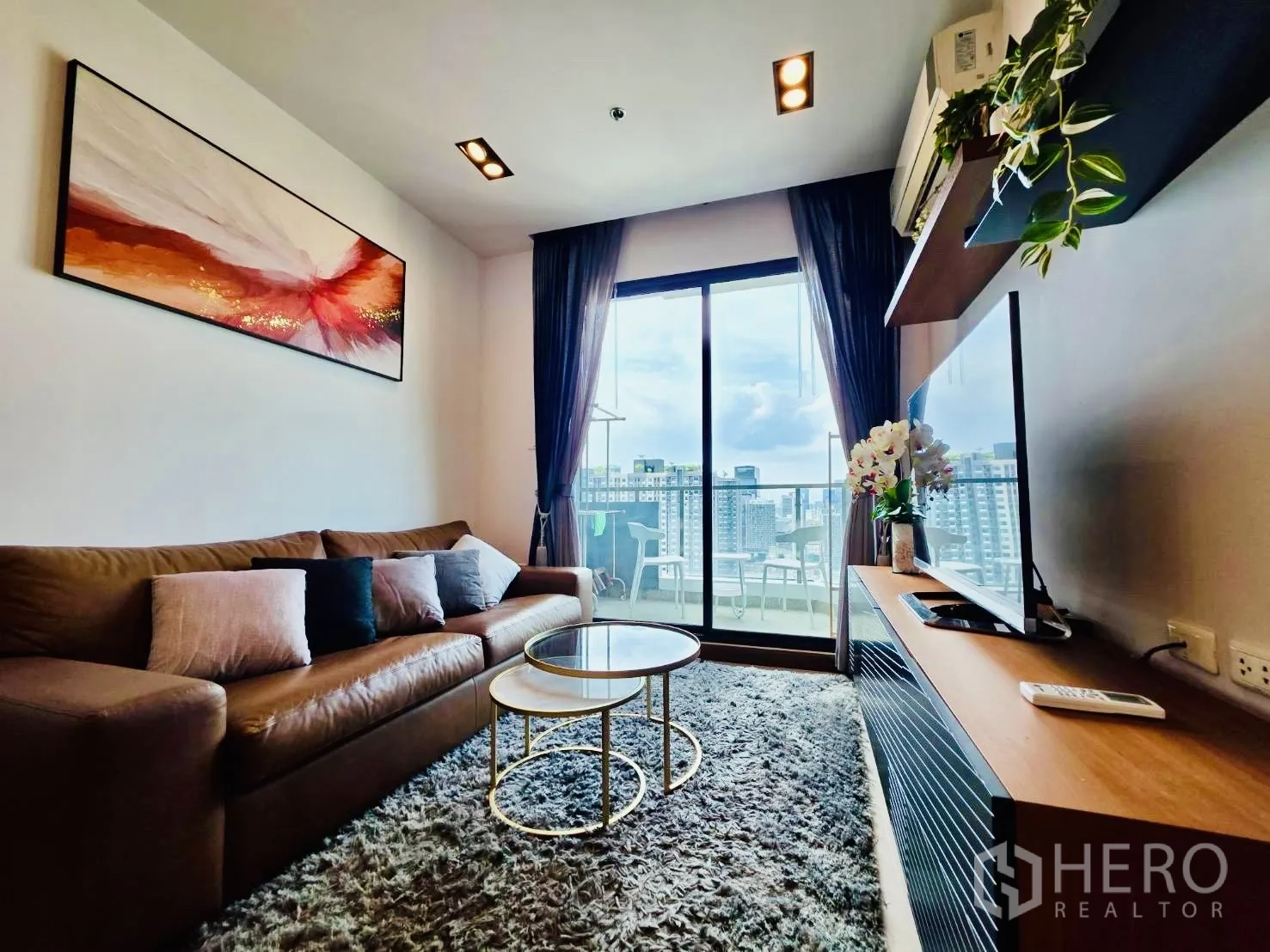 คอนโด for rent in Huai Khwang, Bangkok - ห้องนั่งเล่นอบอุ่นด้วยโซฟาหนังและโต๊ะกลางซ้อน พร้อมประตูกระจกบานเลื่อนออกสู่ระเบียงวิวเมือง