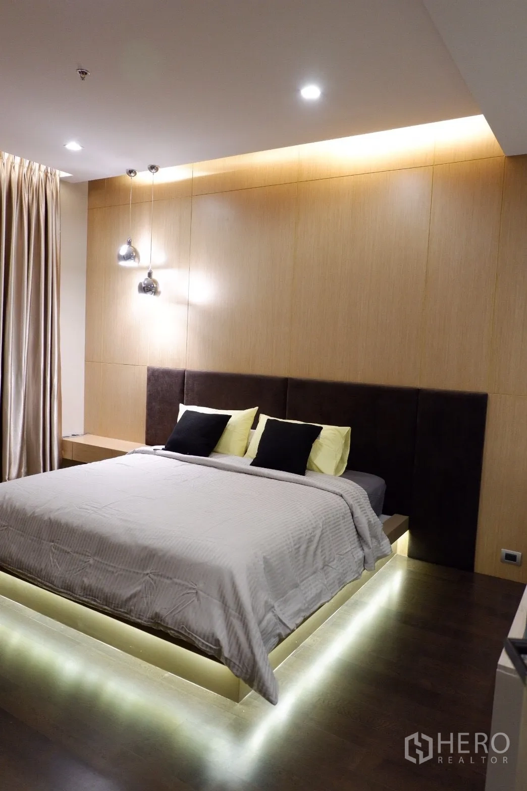 คอนโด ให้เช่าในWatthana, Bangkok - ห้องนอนหลักเตียงแพลตฟอร์มไฟ LED ใต้เตียง ผนังลายไม้ โคมไฟแขวน และพื้นไม้โทนเข้ม