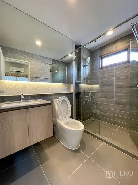 Detached House for rent in Bang Kapi, Bangkok - Contemporary bathroom with vanity, toilet and walk-in shower under strip lighting.