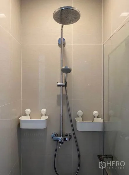 Condominium for rent in Khlong Toei, Bangkok - Tiled shower with rainfall head, handheld sprayer, and wall caddies.