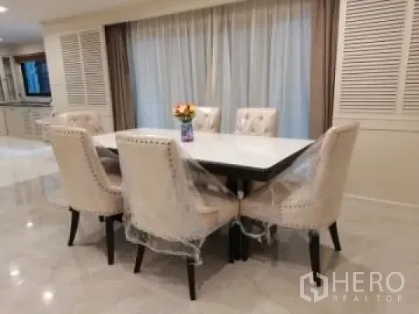 Apartment for rent in Watthana, Bangkok - Bright dining area with a white table and six upholstered chairs, glossy tile floor and full-length curtains.