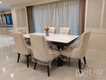 Apartment for rent in Watthana, Bangkok - Bright dining area with a white table and six upholstered chairs, glossy tile floor and full-length curtains.