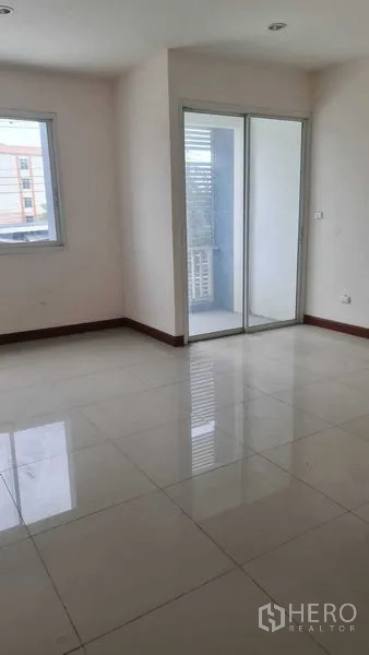 Townhouse for  in Lam Luk Ka, Pathum Thani - Sunlit room with glossy tile floor and balcony access via sliding doors.