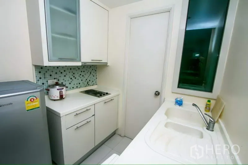 Condominium for rent in Ratchathewi, Bangkok - Compact galley kitchen with mosaic tile backsplash, white cabinetry, sink and door to utility area.