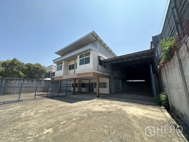 Warehouse for rent in Bueng Kum, Bangkok - Driveway view of warehouse showing ample parking and covered loading entrance on the right.