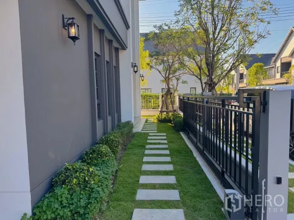 Detached House for rent or sale in Bang Phli, Samut Prakan - Side garden with stepping-stone path, lawn and black metal fence.