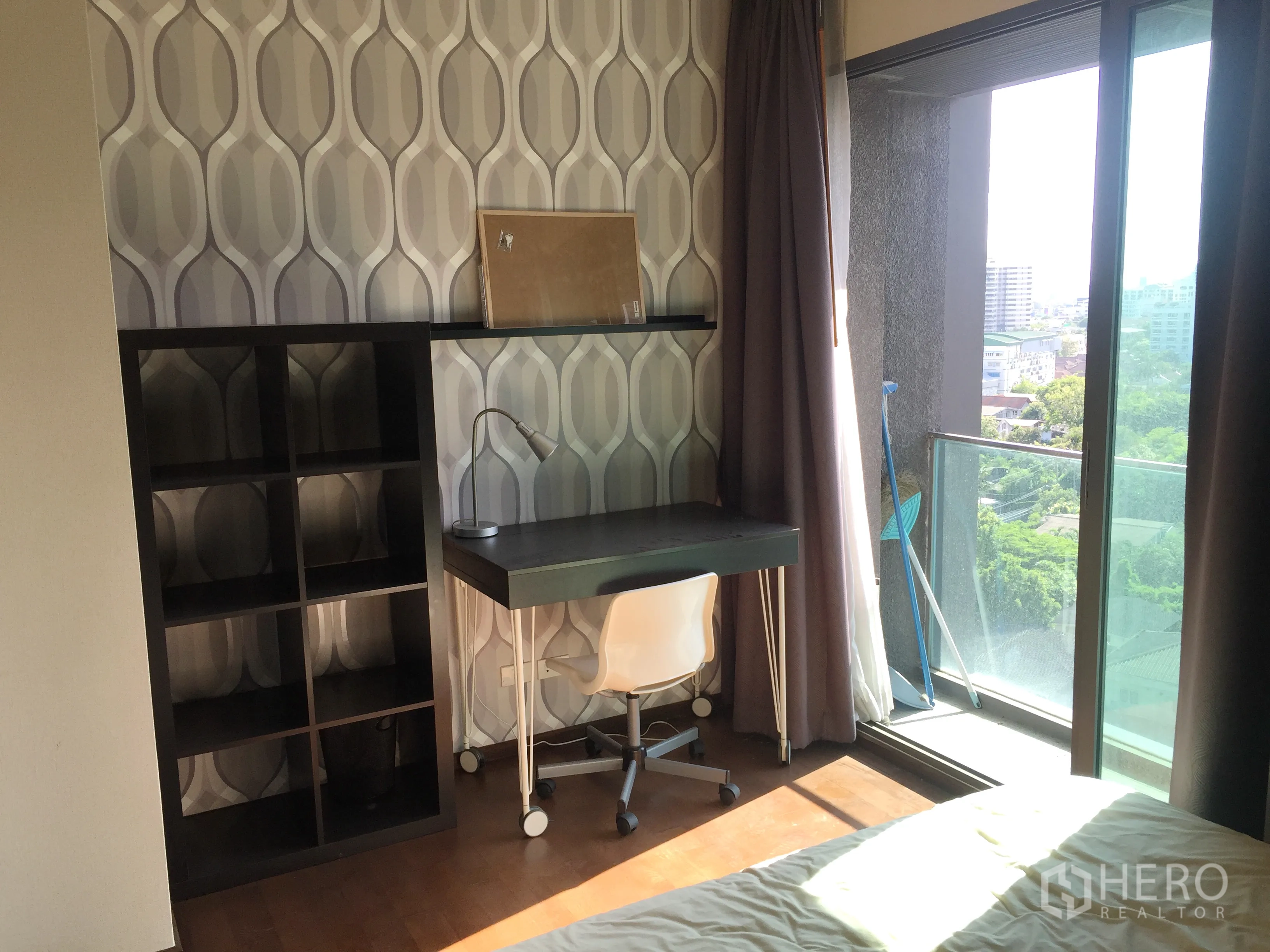 Condominium for rent in Khlong Toei, Bangkok - Bedroom with study desk and shelving beside a balcony door overlooking city greenery.
