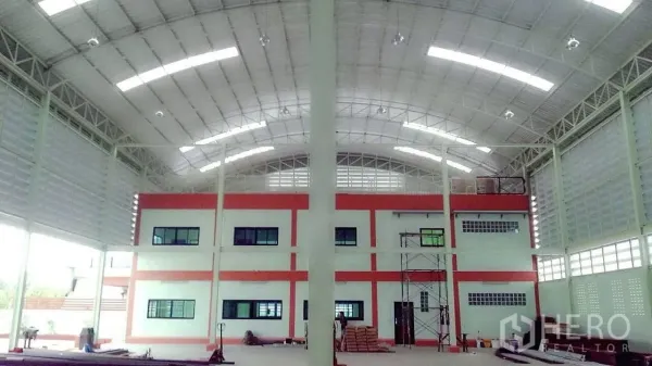 Factory for sale in Pathum Thani - Spacious factory interior with high arched roof, steel columns and a two‑storey office block.
