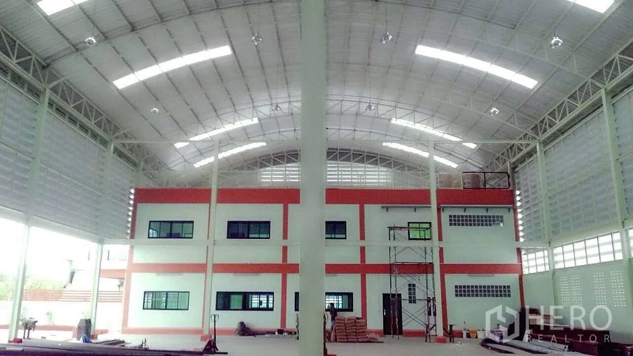 Factory for sale in Pathum Thani - Spacious factory interior with high arched roof, steel columns and a two‑storey office block.