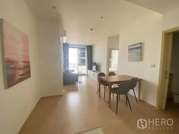 公寓 出租在Watthana, Bangkok - 开放式餐客区，四人餐桌，浅木地板，尽头为通向阳台的大玻璃门。