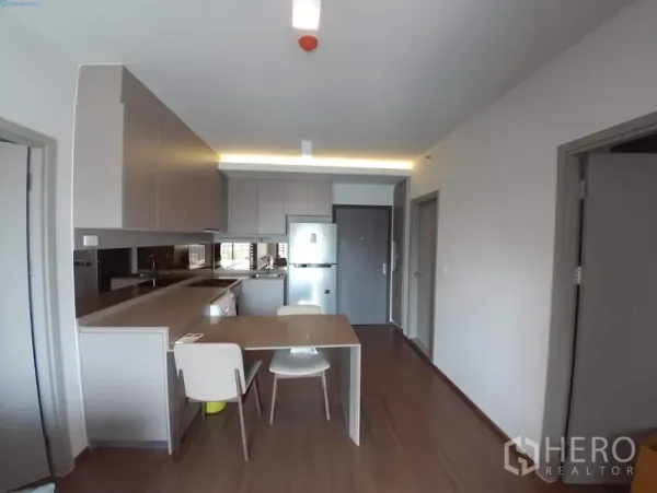 Condominium for rent in Phra Khanong, Bangkok - Open-plan kitchen with built-in cabinets, long countertop, dining table and fridge in a modern condo.