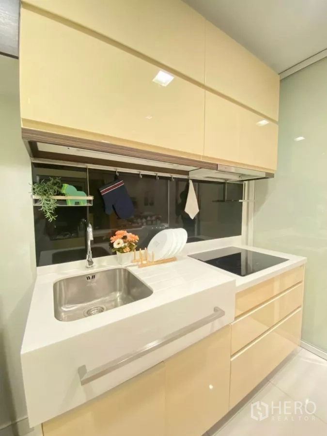 Condominium for rent in Phra Khanong, Bangkok - Compact modern kitchen with sink, induction cooktop, and glossy cabinets.