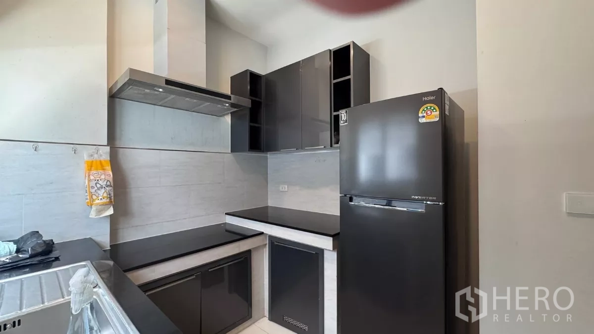 Detached House for rent or sale in Saphan Sung, Bangkok - Compact modern kitchen with glossy black cabinetry, stainless range hood, refrigerator and tiled backsplash.