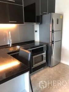 Condominium for rent or sale in Khlong Toei, Bangkok - Modern kitchenette with glossy black counters, stainless refrigerator and microwave.