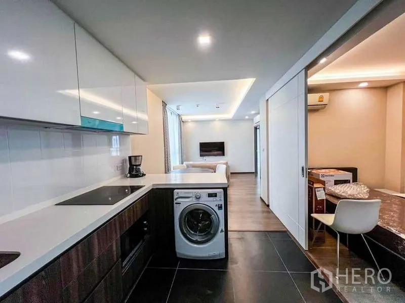 คอนโด ขายในHuai Khwang, Bangkok - มุมมองจากครัวไปยังห้องนั่งเล่น พร้อมเคาน์เตอร์เพนนินซูลา เครื่องซักผ้า และประตูบานเลื่อนไปยังอีกห้อง