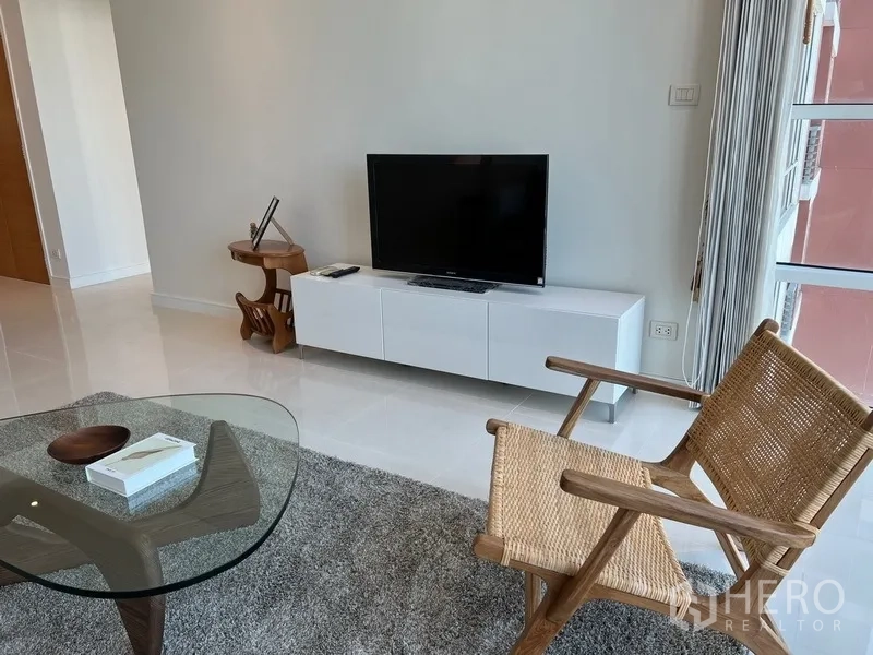 公寓 出租在Watthana, Bangkok - 客厅电视柜与藤编休闲椅，地毯营造温馨氛围。