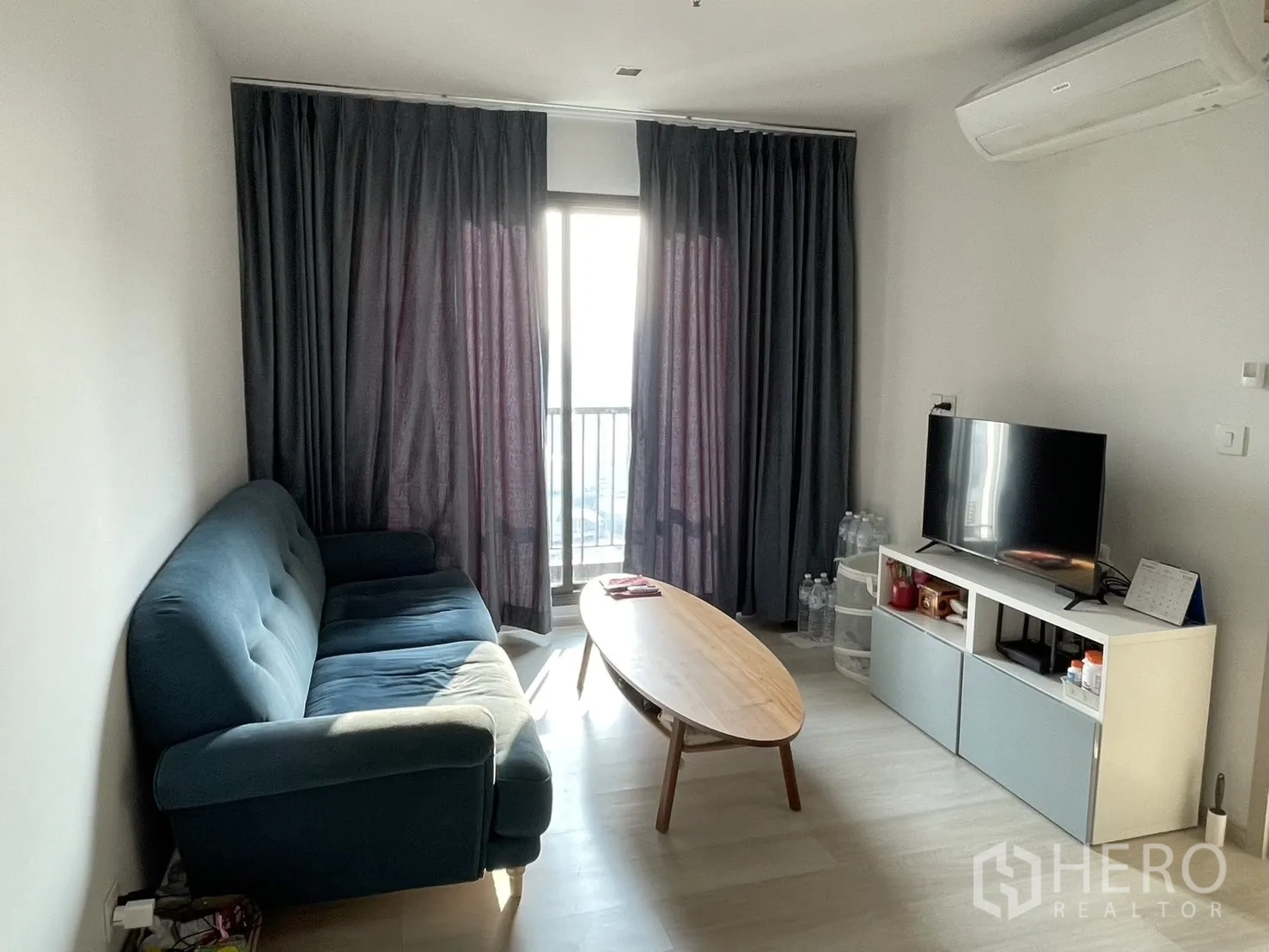 คอนโด for rent in Pathum Wan, Bangkok - ห้องนั่งเล่นโซฟาสีน้ำเงิน ชั้นวางทีวี และประตูสู่ระเบียงพร้อมผ้าม่านสูง