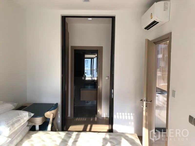 Condominium for rent in Watthana, Bangkok - Bedroom with a small desk and doorway to the bathroom, featuring light wood floors and air conditioning.