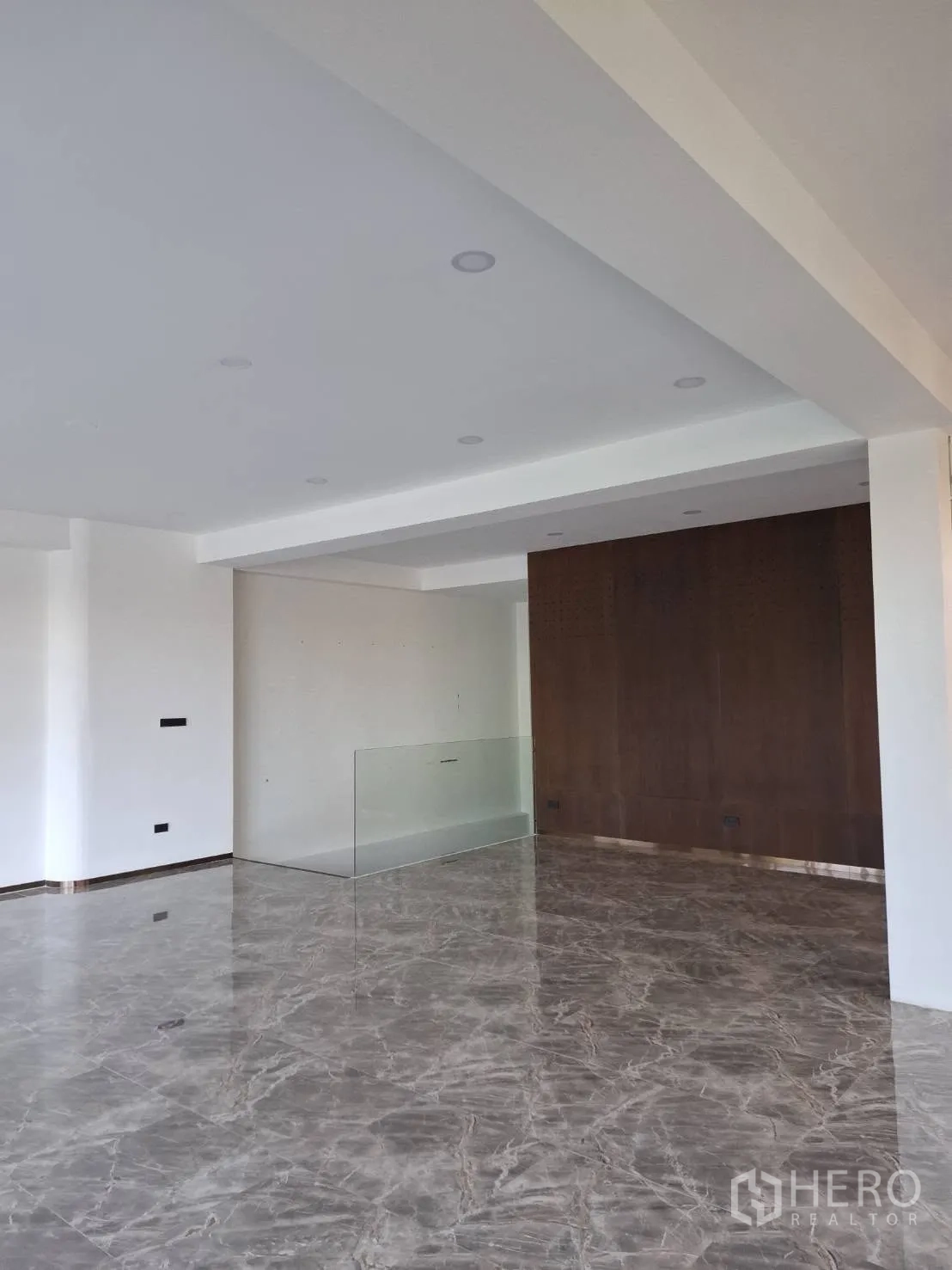 Retail Space for rent in Watthana, Bangkok - Open-plan retail interior with polished stone floors, recessed lighting, a wood accent wall and glass railing.