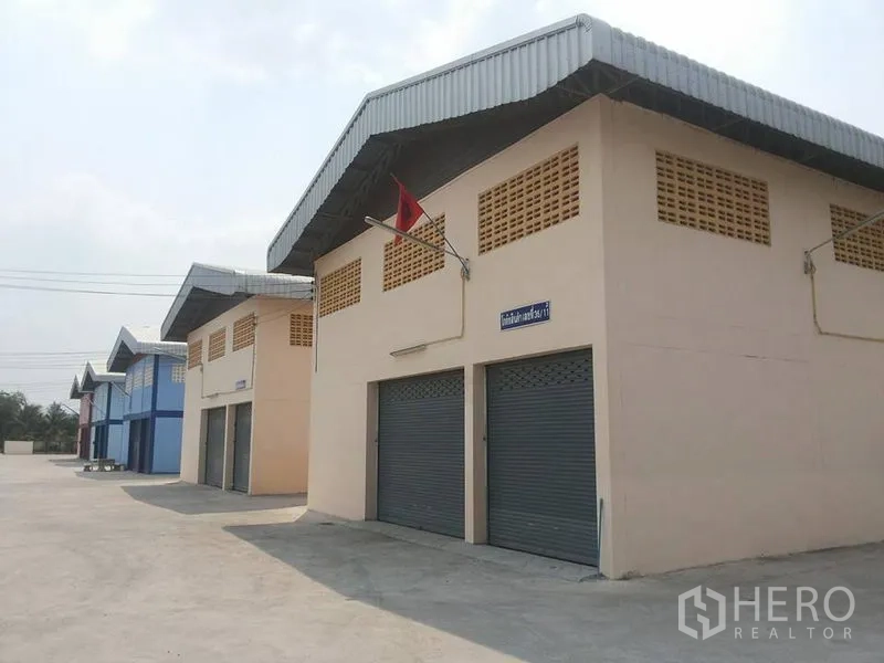 Factory for rent in Lat Lum Kaeo, Pathum Thani - Row of light-industrial warehouses with roller shutter doors and ventilated gables facing a clean paved yard.