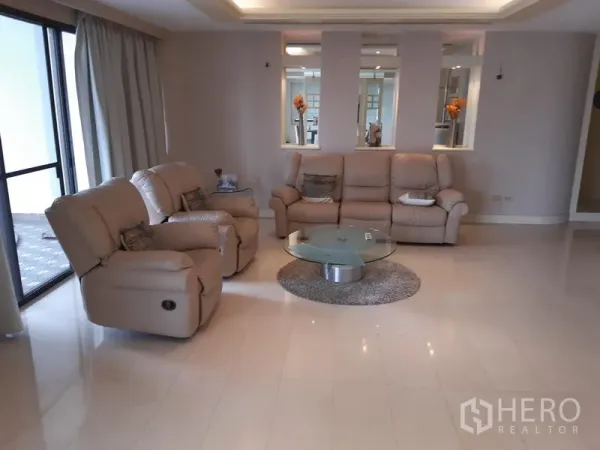 Condominium for rent in Khlong Toei, Bangkok - Living room with beige recliner sofas, glass coffee table and access to a balcony.