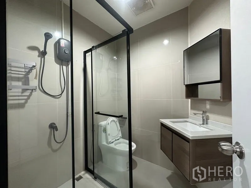 Townhouse for rent or sale in Phra Khanong, Bangkok - Modern bathroom with glass-enclosed shower and wall-mounted vanity.
