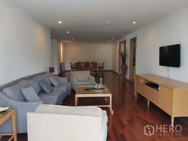 Condominium for rent in Khlong Toei, Bangkok - Open-plan living and dining space with sofas, a TV wall, and glossy hardwood floors.