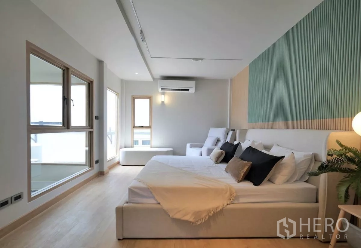 Townhouse for rent in Watthana, Bangkok - Spacious master bedroom with seating area, air conditioning and a textured green feature wall.