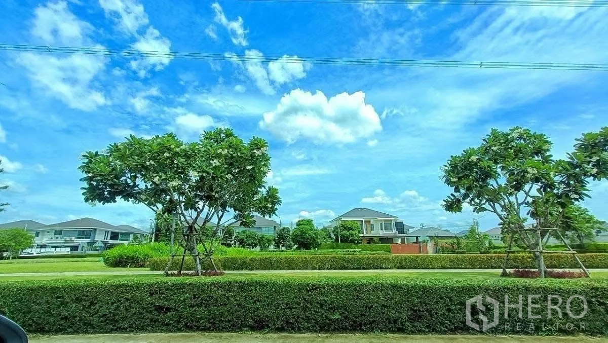 Detached House for rent in Lat Krabang, Bangkok - Tree-lined neighborhood green space with contemporary houses under a blue sky.