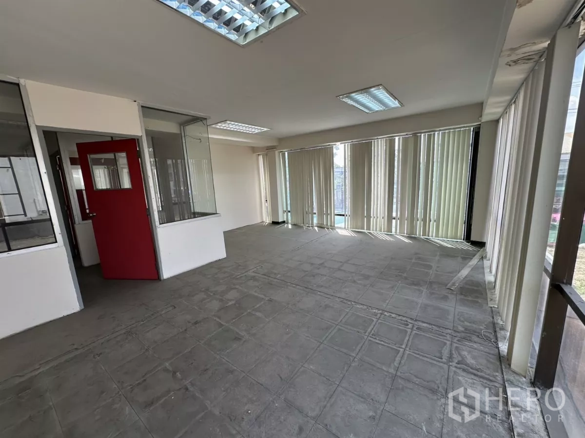 Warehouse for rent in Suan Luang, Bangkok - Office area with red door, glass partitions, fluorescent lighting, and windows with blinds.