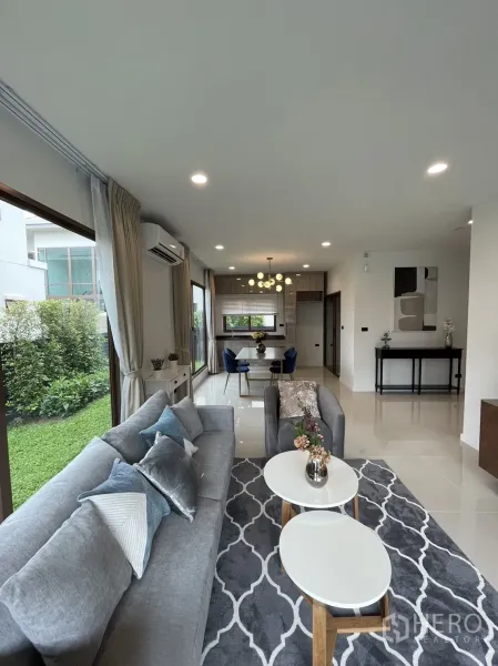 Detached House for rent in Bang Kapi, Bangkok - Open-plan living and dining area with large windows, grey sofa, rug, and garden view.