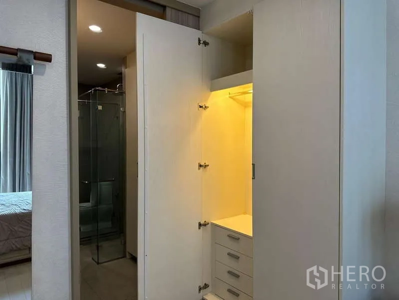 公寓 出租或出售 - 打开的照明衣柜，旁为带玻璃隔断的浴室。