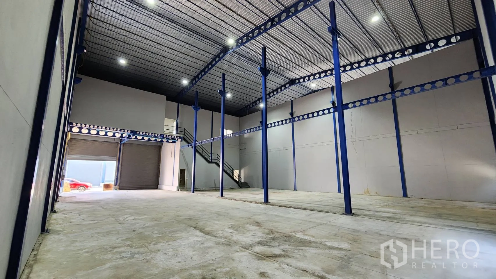 Warehouse for rent in Krathum Baen, Samut Sakhon - High-clear warehouse interior with blue steel columns, polished concrete floor, and large roller shutter next to office staircase.