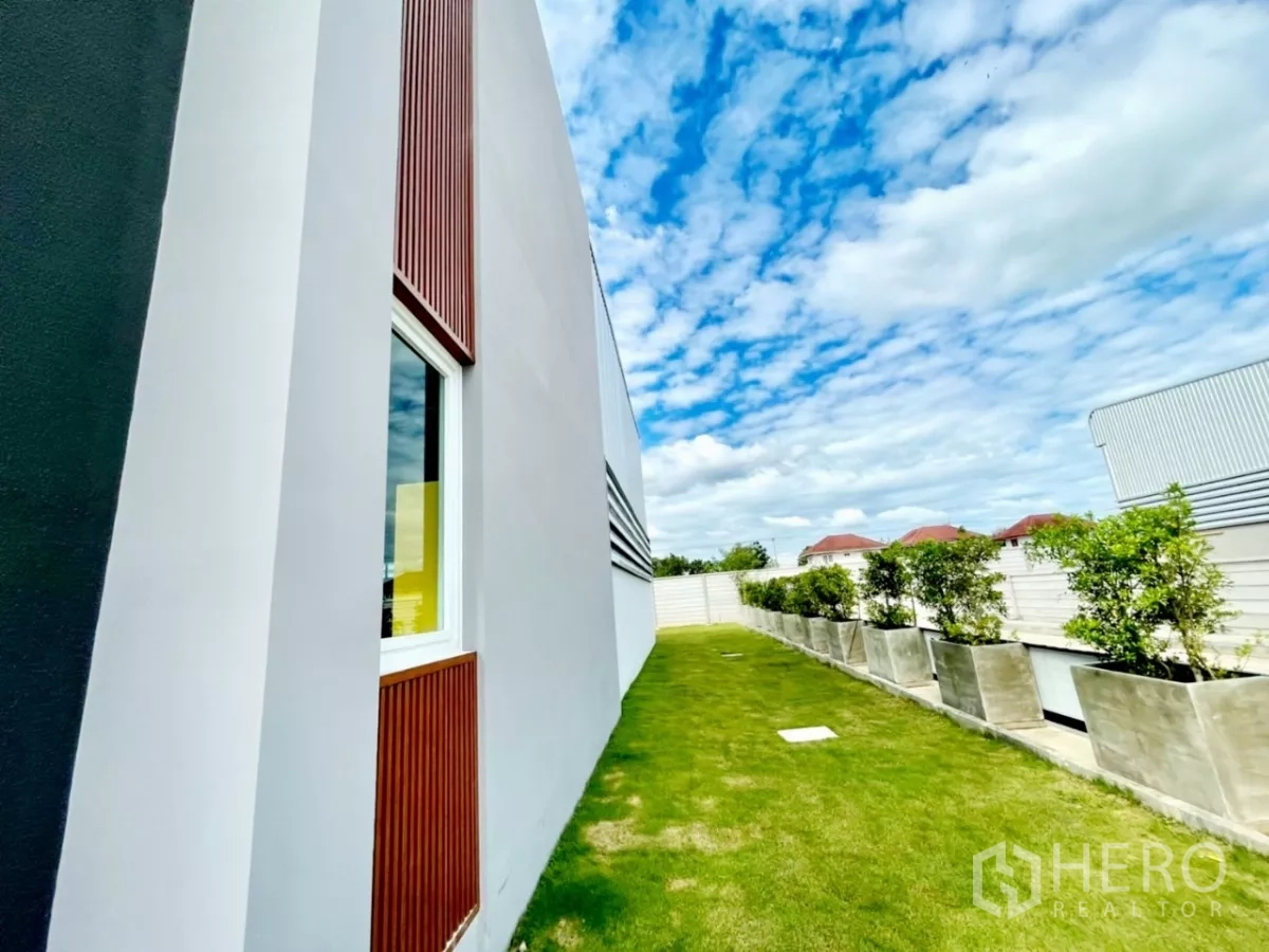 货栈 出售在Lam Luk Ka, Pathum Thani - 办公楼与仓库侧立面，草坪、花盆与围墙一线排开。