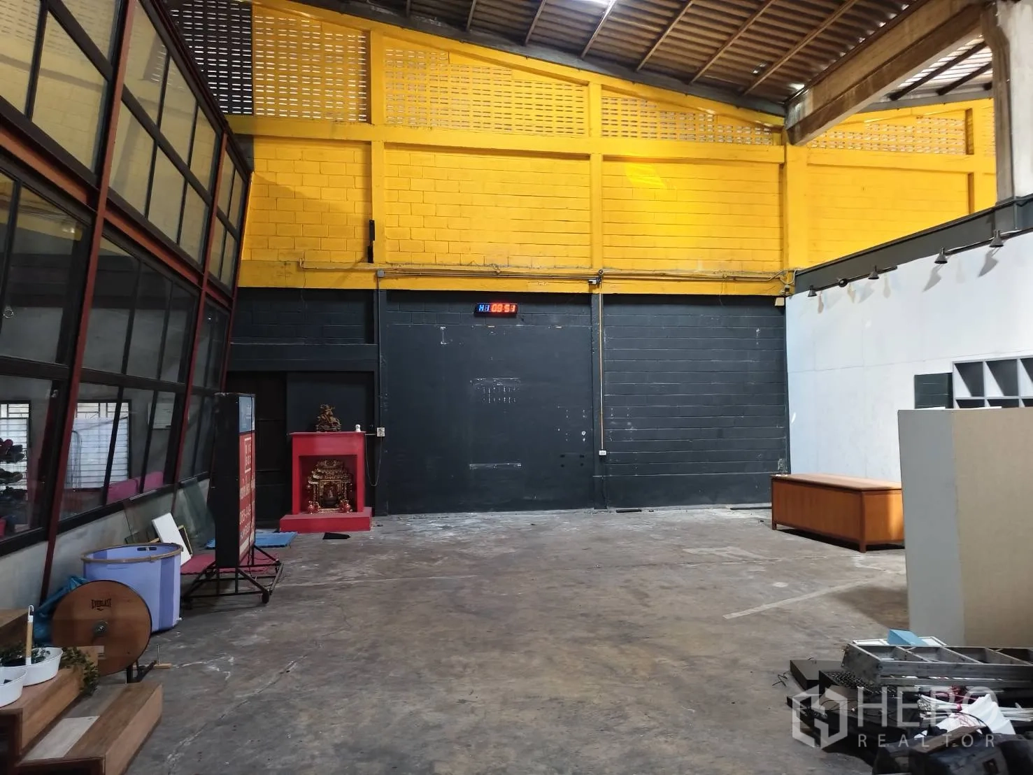货栈 出租在Khlong Toei, Bangkok - 黄色点缀墙、黑色卷帘门与开阔仓库地面。