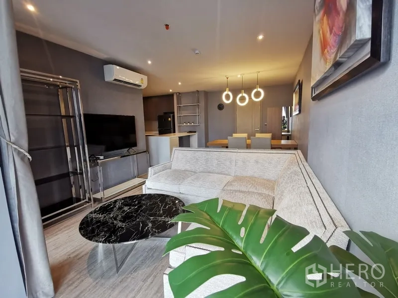 公寓 出租或出售在Watthana, Bangkok - 现代开放式客餐厅，L型沙发、黑色大理石茶几、壁挂电视与环形吊灯。