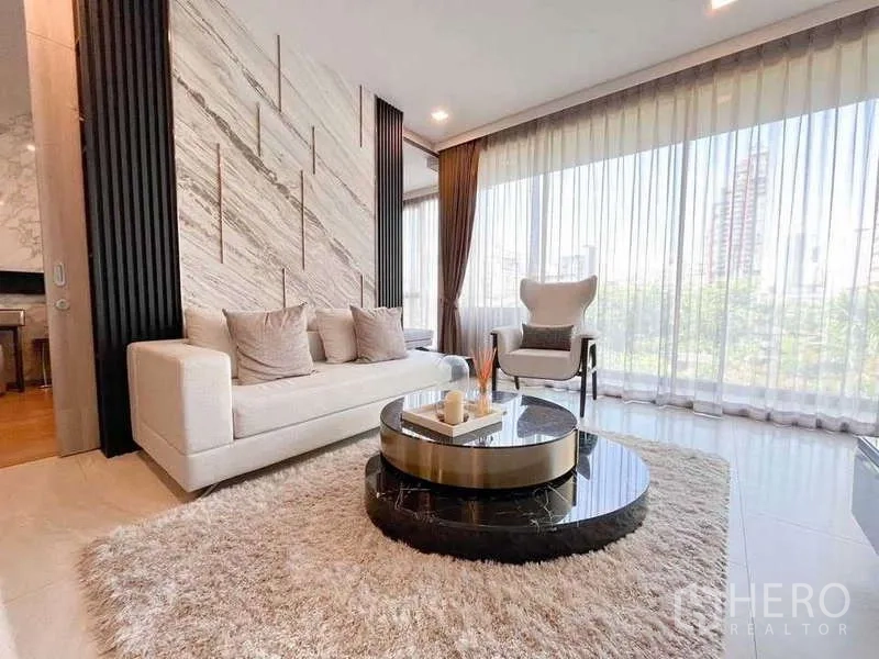 公寓 出租在Watthana, Bangkok - 采光充足的客厅，石材背景墙、转角落地窗与现代沙发。